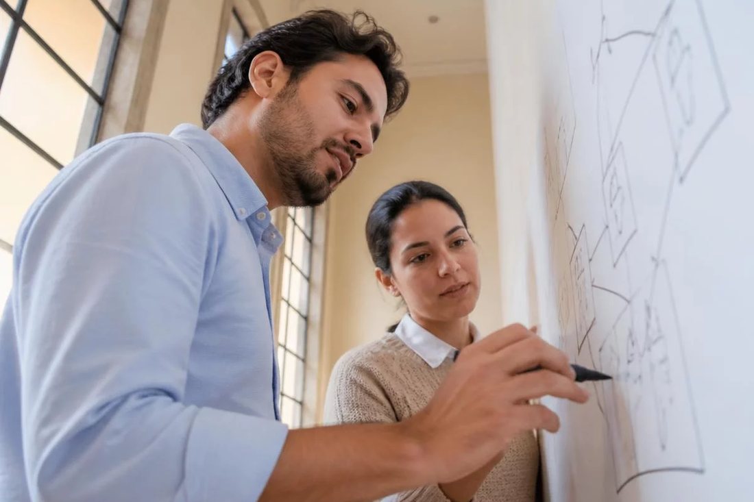 Dois alunos em pé diante do quadro branco, riscando a ordem em que o argumento será apresentado